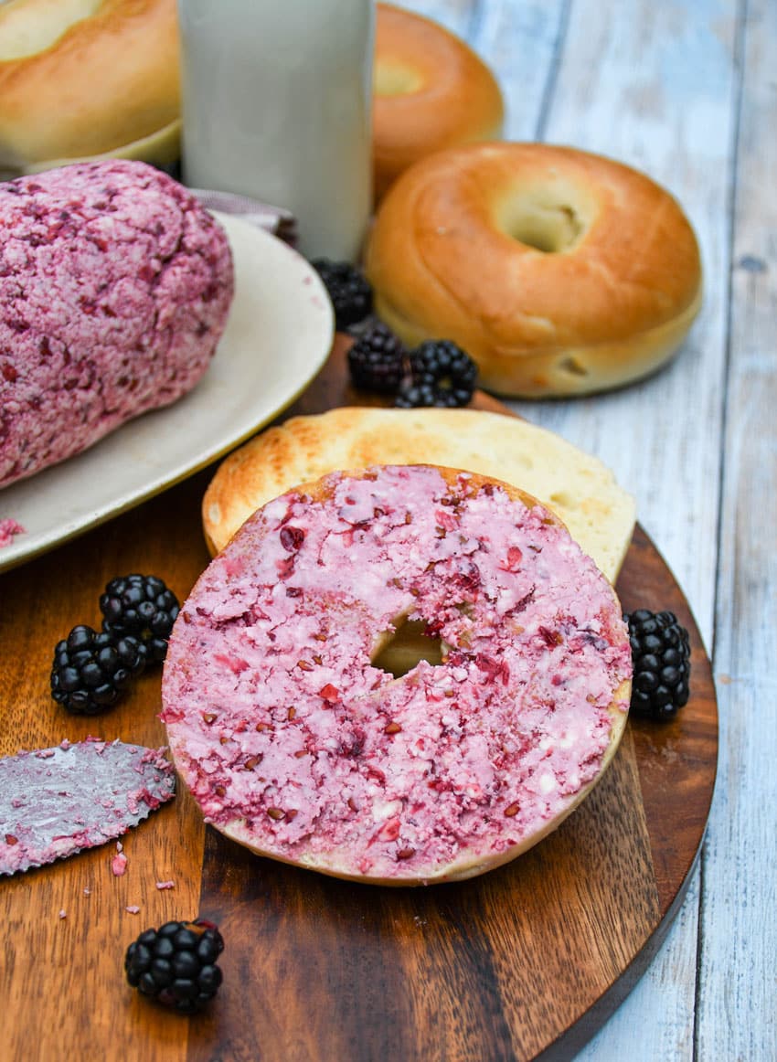 a toasted bagel spread with fresh berry butter resting on a wooden cutting board