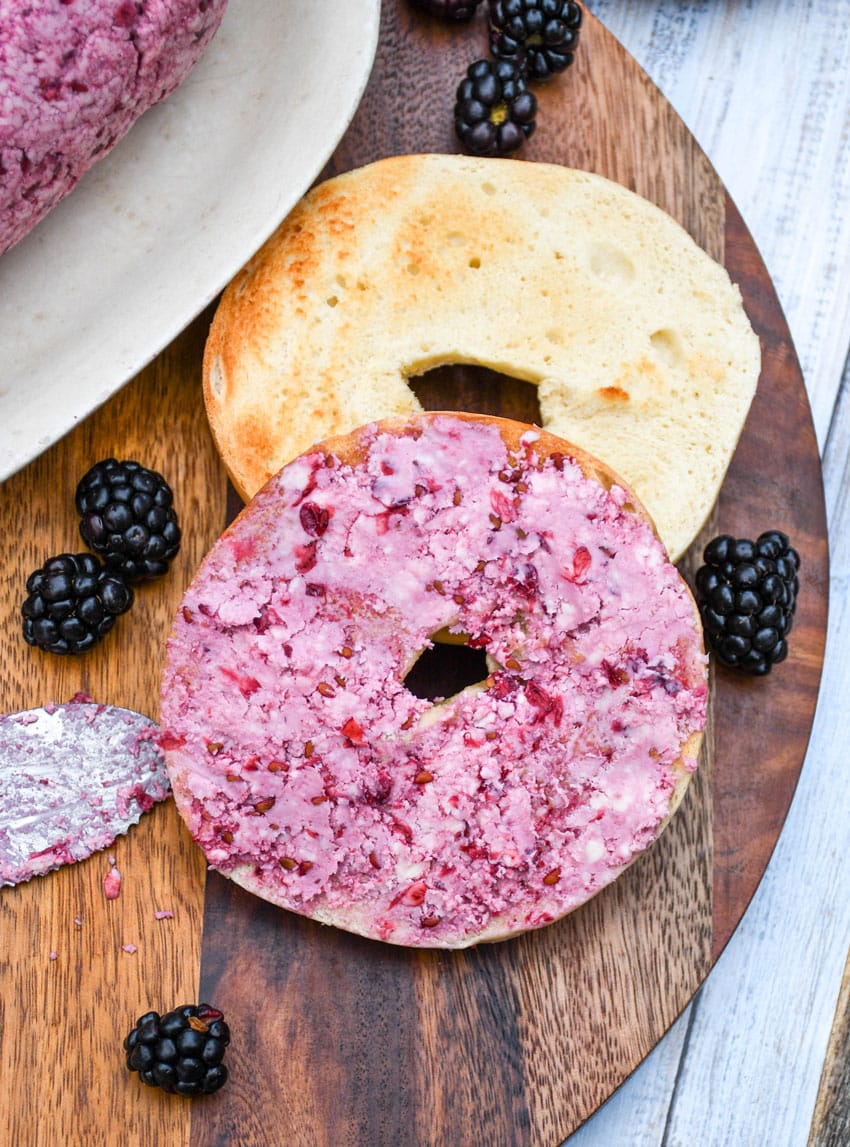 a toasted bagel spread with fresh berry butter resting on a wooden cutting board