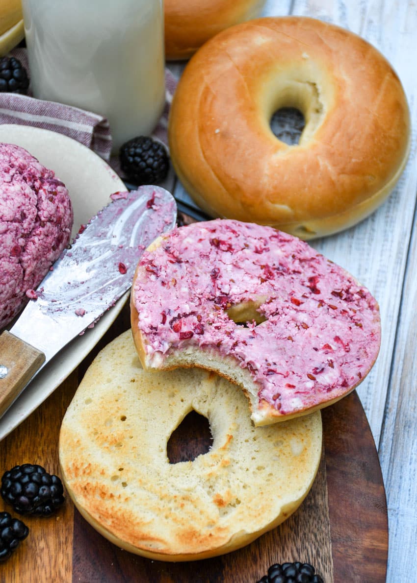 a toasted bagel spread with fresh berry butter resting on a wooden cutting board