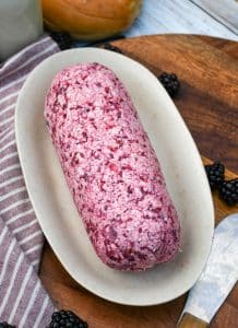 a log of whipped blackberry butter on a small dish on a wooden cutting board