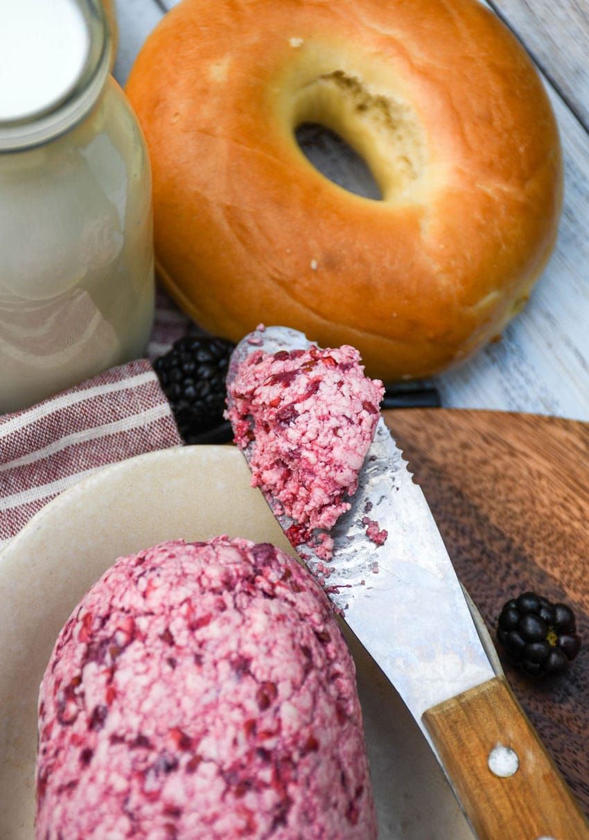 a butter spreader holding a scoop of homemade blackberry butter resting on the edge of a small white dish