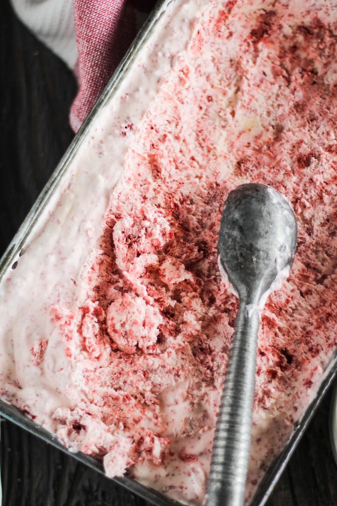 no churn red velvet ice cream in a metal loaf pan with a silver ice cream scooper