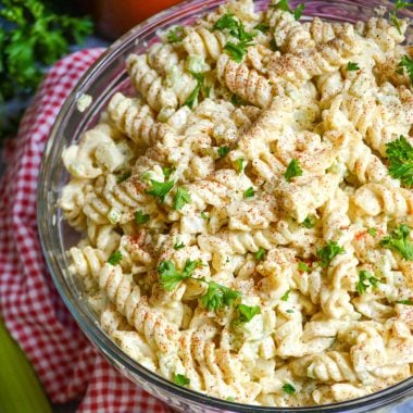 creamy macaroni salad in a glass bowl on top of a red checkered cloth napkin