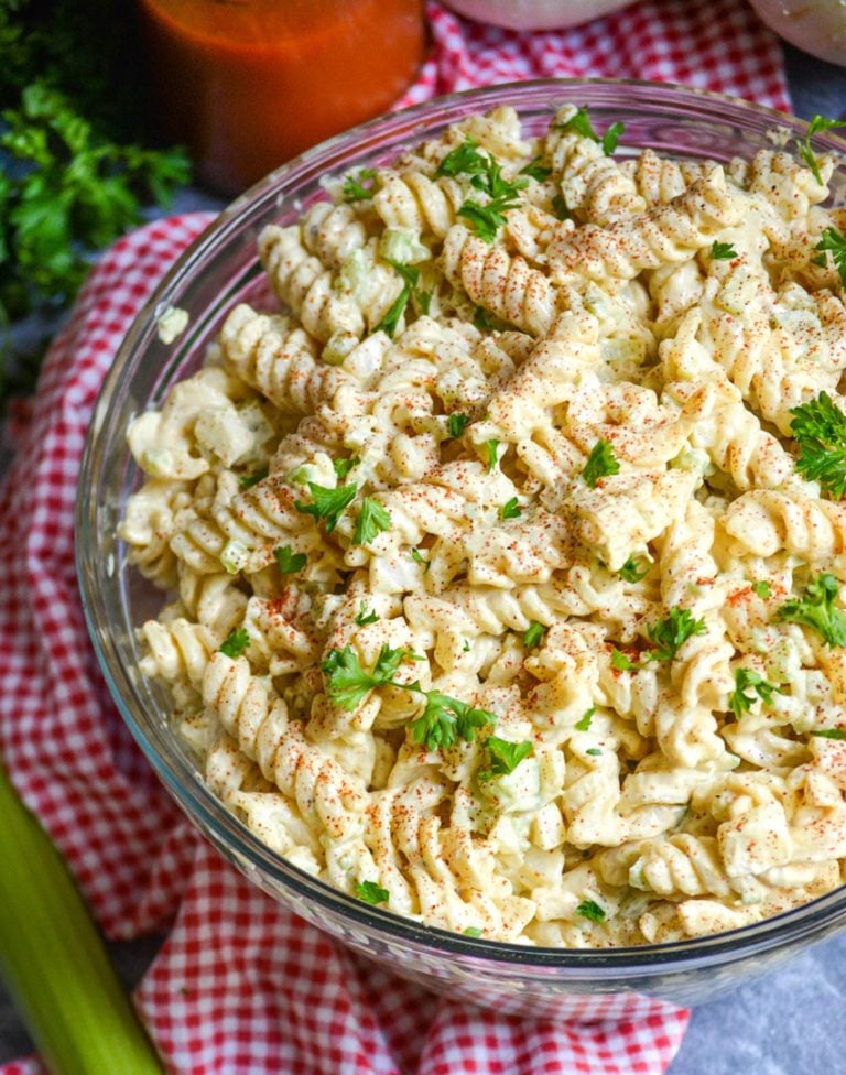 creamy macaroni salad in a glass bowl on top of a red checkered cloth napkin