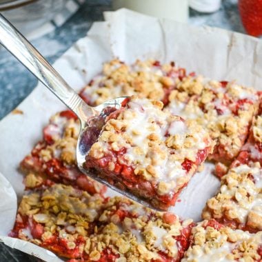 healthy strawberry oat bars on parchment paper and cut into squares with the center square held aloft on a silver spatula