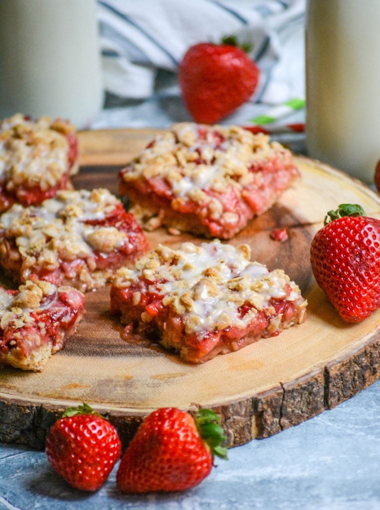 glazed strawberry oat bars sliced into squares and served on a wooden cutting board with ripe strawberries and glasses of milk in the background