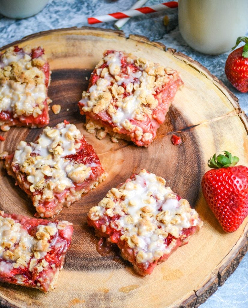 strawberry oat bars cut into squares and shown on a wooden cutting board with fresh strawberries in the background