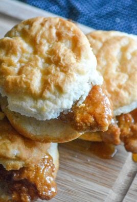 sweet & spicy glazed chicken tenders sandwiched in buttermilk biscuits on a wooden cutting board