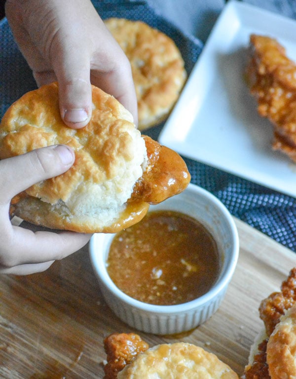 sweet & spicy glazed chicken tenders sandwiched in buttermilk biscuits on a wooden cutting board