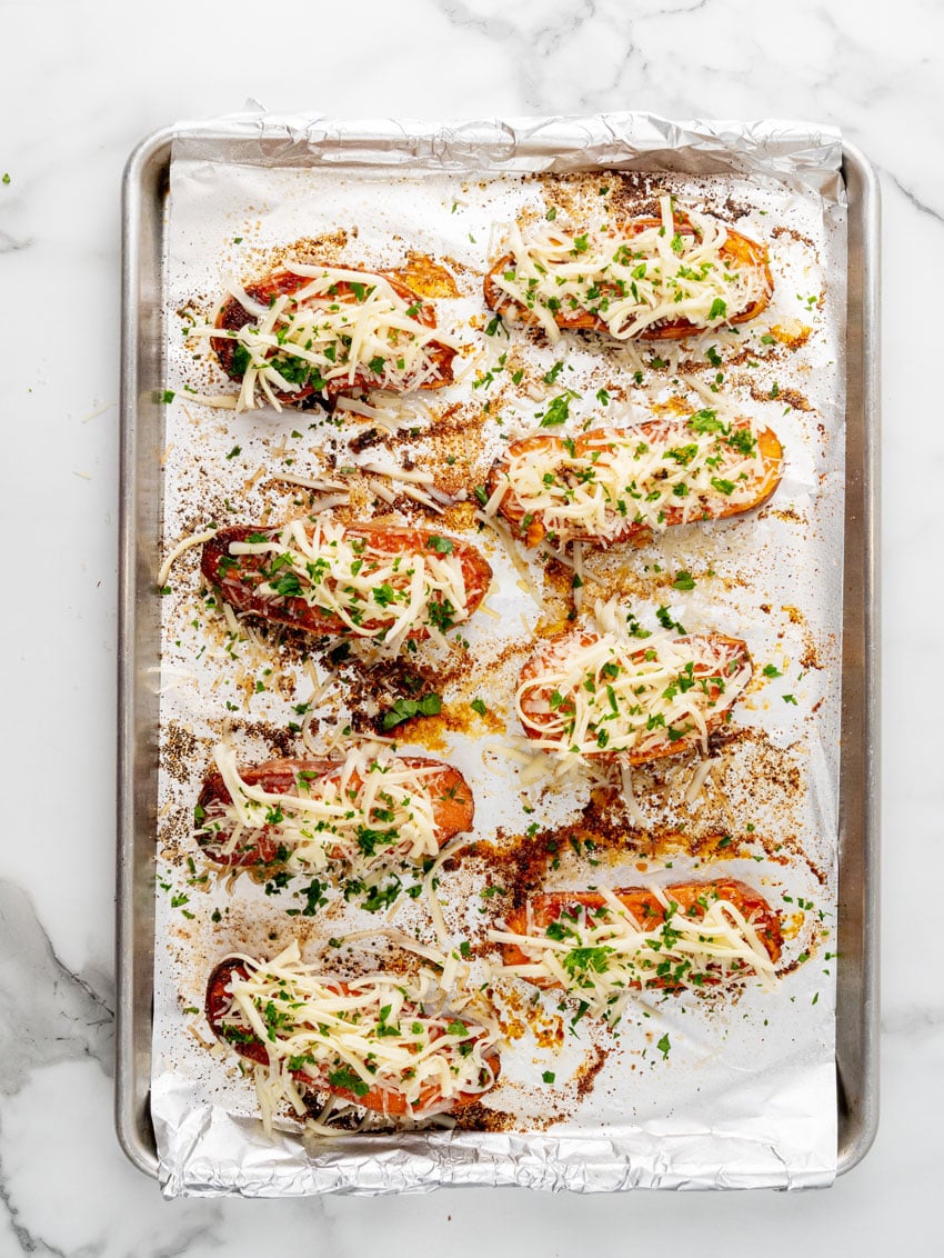 garlic butter brushed roasted sweet potatoes topped with shredded mozzarella cheese on a foil lined baking sheet