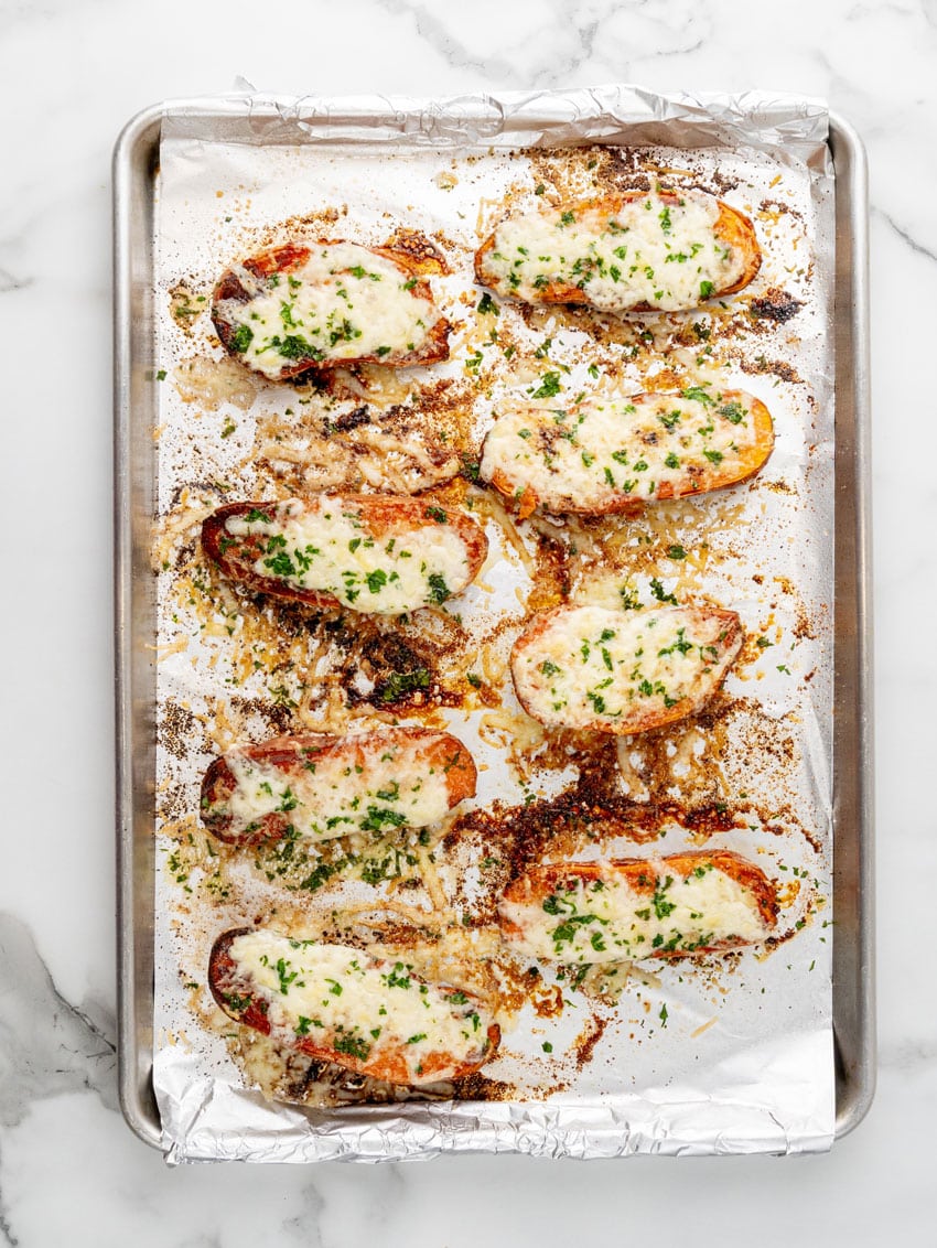 garlic butter brushed roasted sweet potatoes topped with shredded mozzarella cheese on a foil lined baking sheet