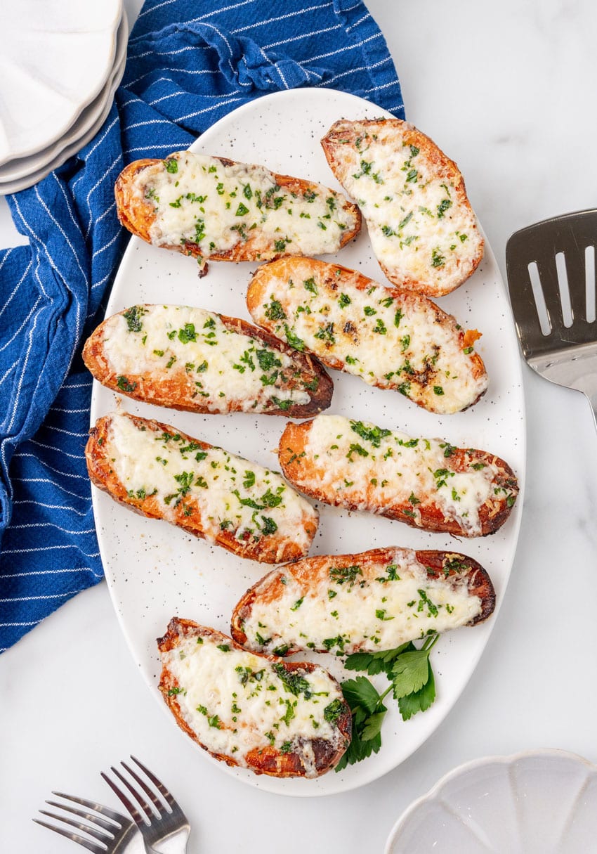 baked cheesy garlic roasted sweet potatoes on a white serving platter