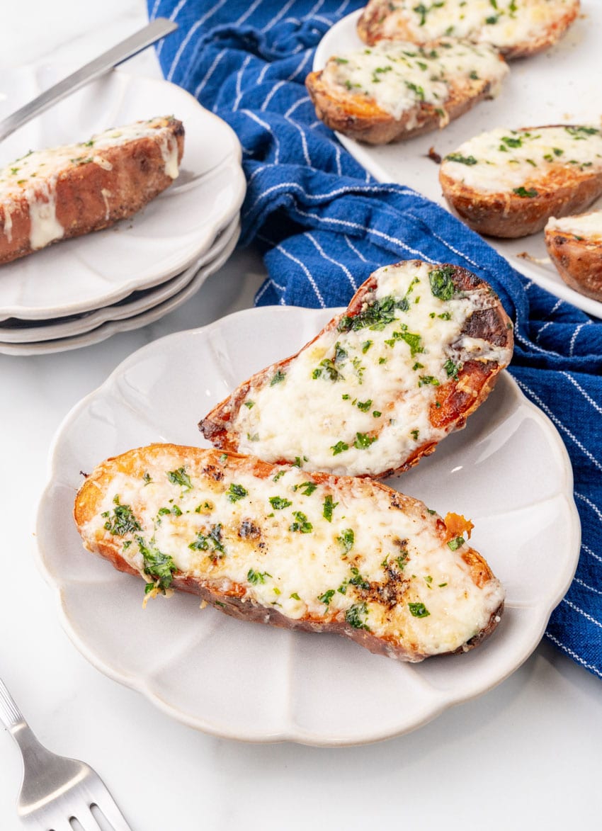 baked cheesy garlic roasted sweet potato halved on a small white appetizer plate