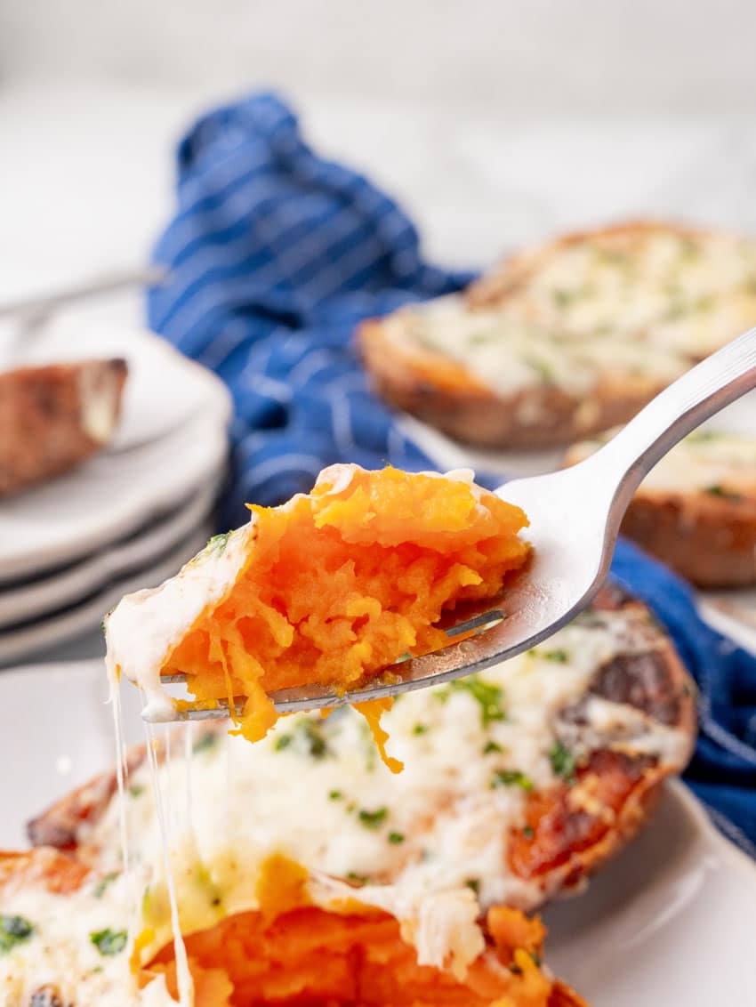 a silver fork holding up a scoop of cheesy roasted sweet potato