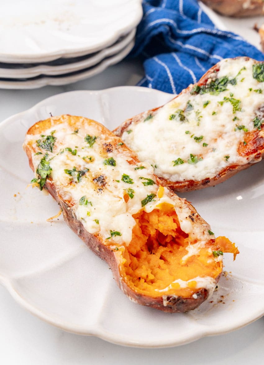 baked cheesy garlic roasted sweet potato halved on a small white appetizer plate