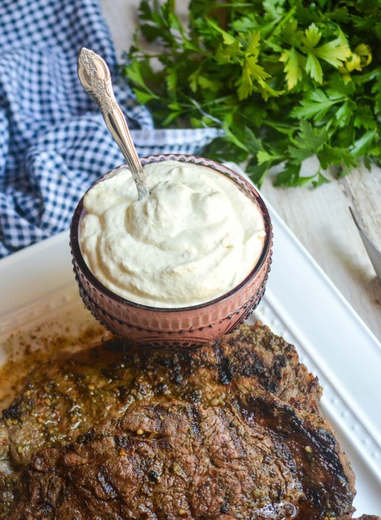 creamy horseradish sauce in a purple glass serving bowl shown with grilled steaks on a white platter