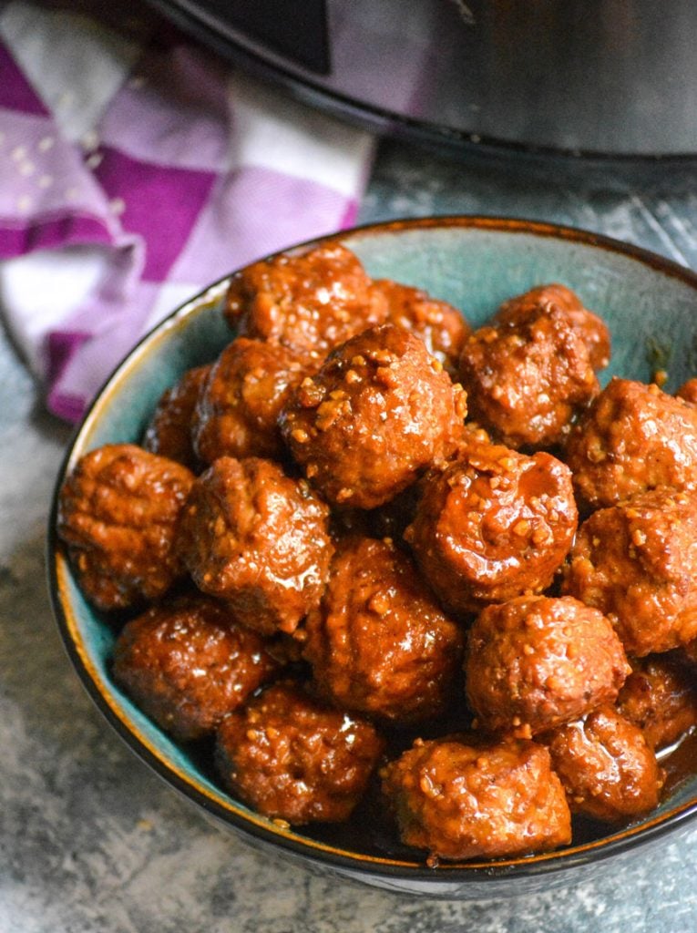 saucy Asian flavored meatballs piled high in a ceramic bowl with a purple and white plaid napkin in the background