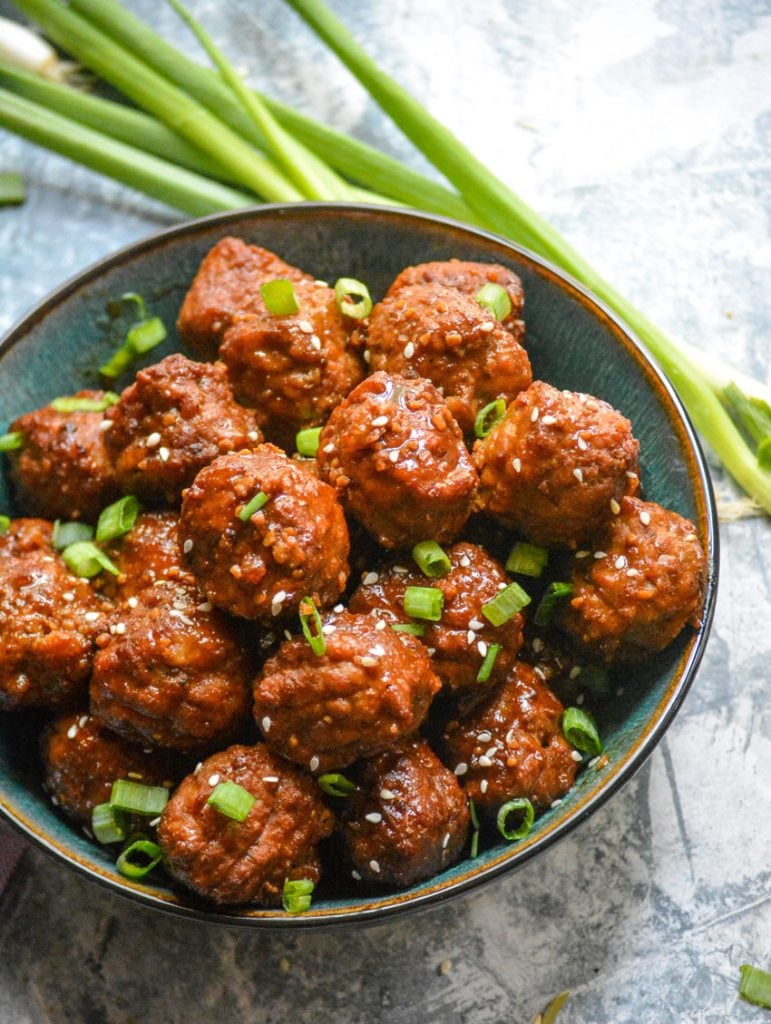 Asian flavored meatballs in a ceramic bowl with a bunch of fresh green onions in the background