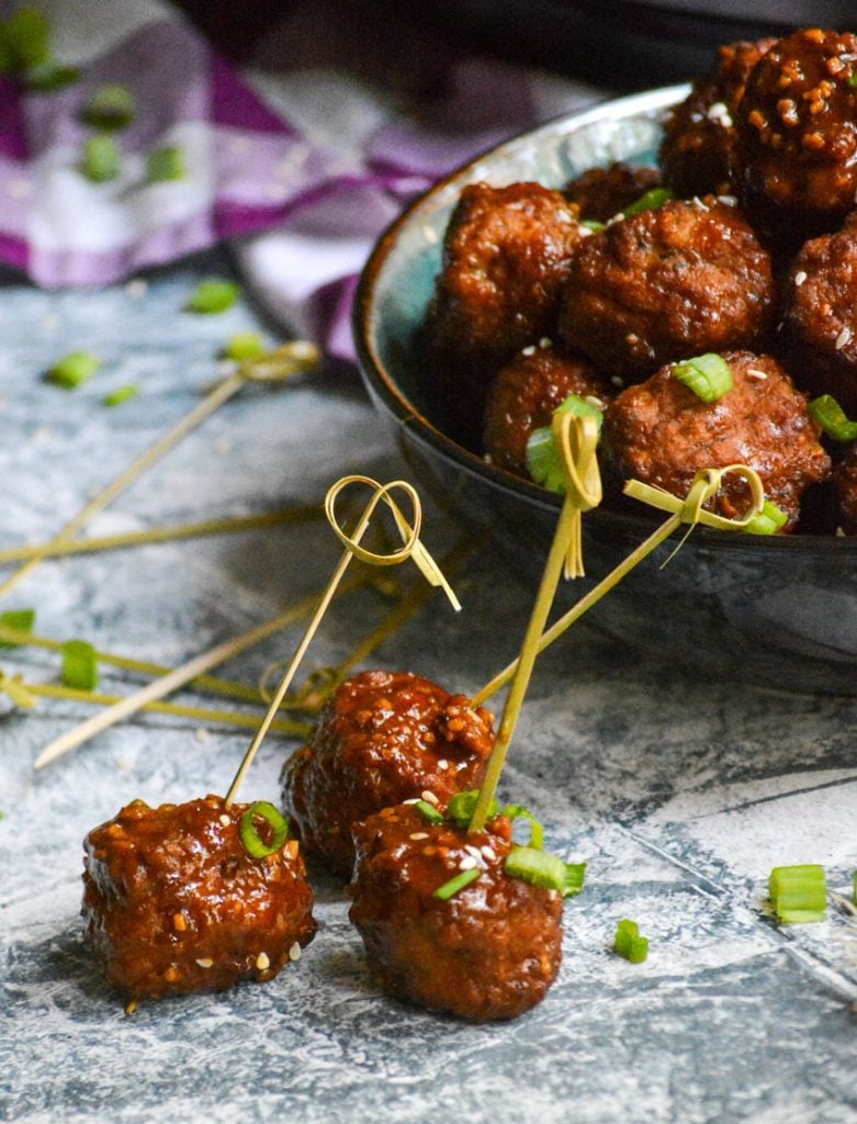 crockpot Asian meatballs with fancy toothpicks stuck in them and more in a blue ceramic bowl in the background