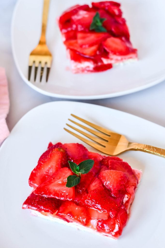 slices of strawberry slab pie on white plates with golden forks and a pink napkin in the background