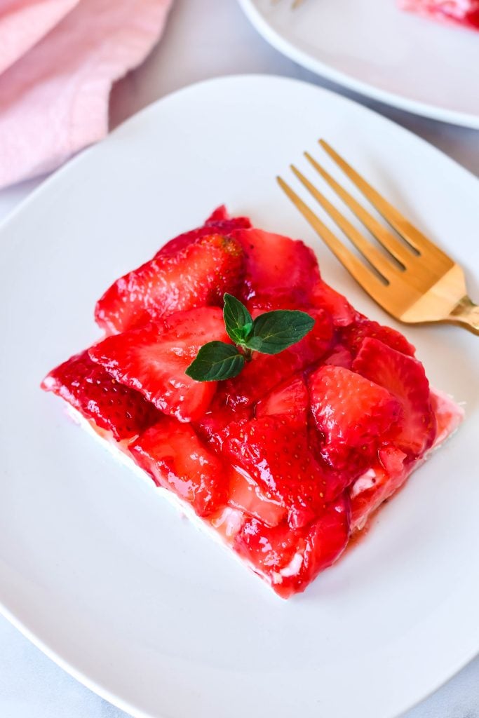 slices of strawberry slab pie on white plates with golden forks and a pink napkin in the background
