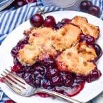 grandma's sweet cherry cobbler on a small white dessert plate with a silver fork resting on the side