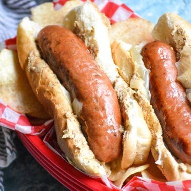 instant pot beer brats stacked in a red picnic basket with pickled onions and potato salad in the background