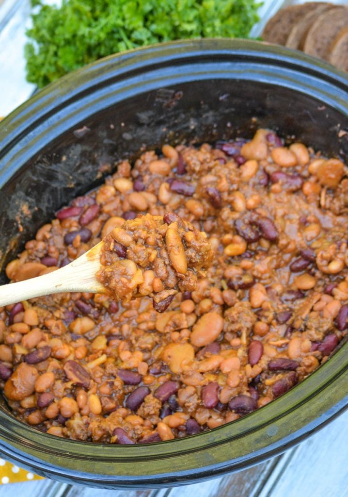 slow cooker cowboy beans in the bowl of crcokpot on a white wooden table