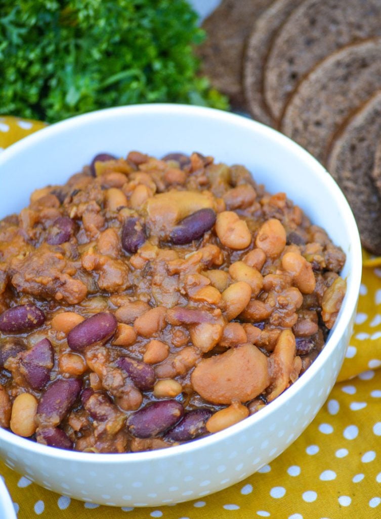 slow cooker cowboy beans in white bowls on a yellow polka dotted cloth napkin