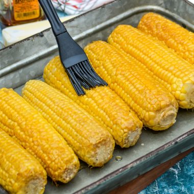 smoked honey butter corn on the cob being rubbed with silicone brush