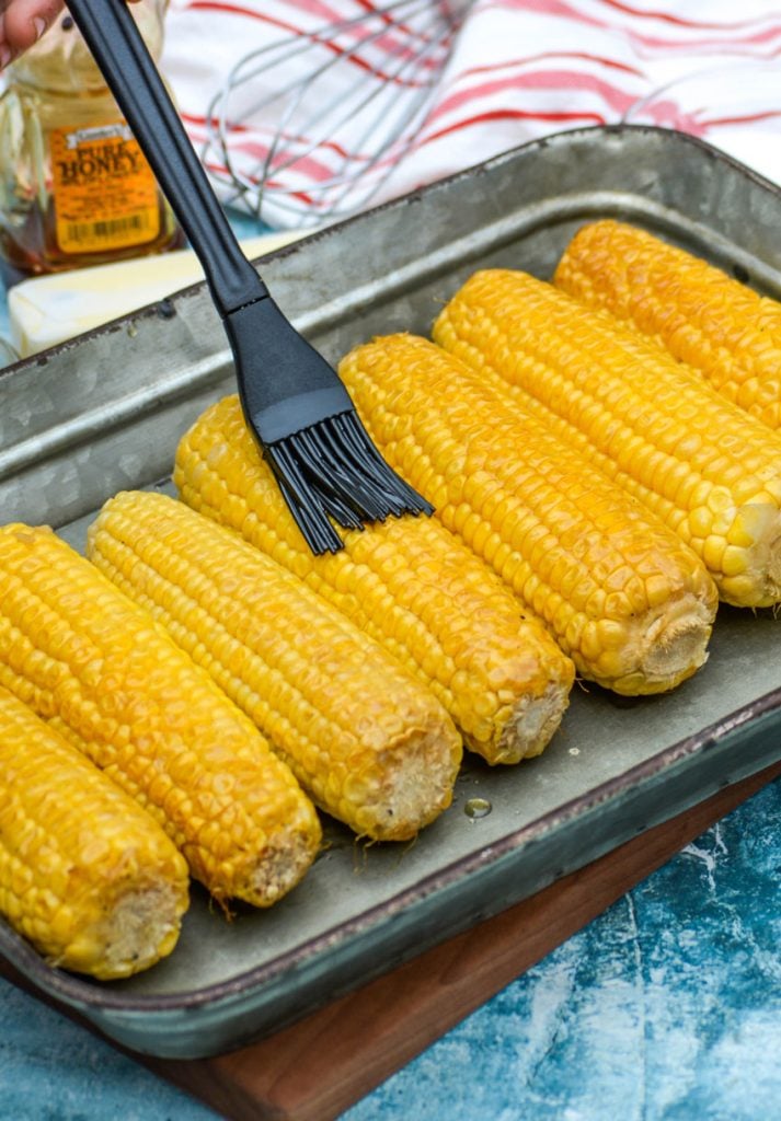 smoked honey butter corn on the cob being rubbed with silicone brush