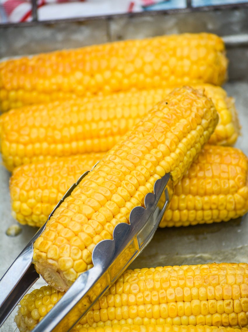 honey glazed smoked corn on the cob held aloft with metal tongs