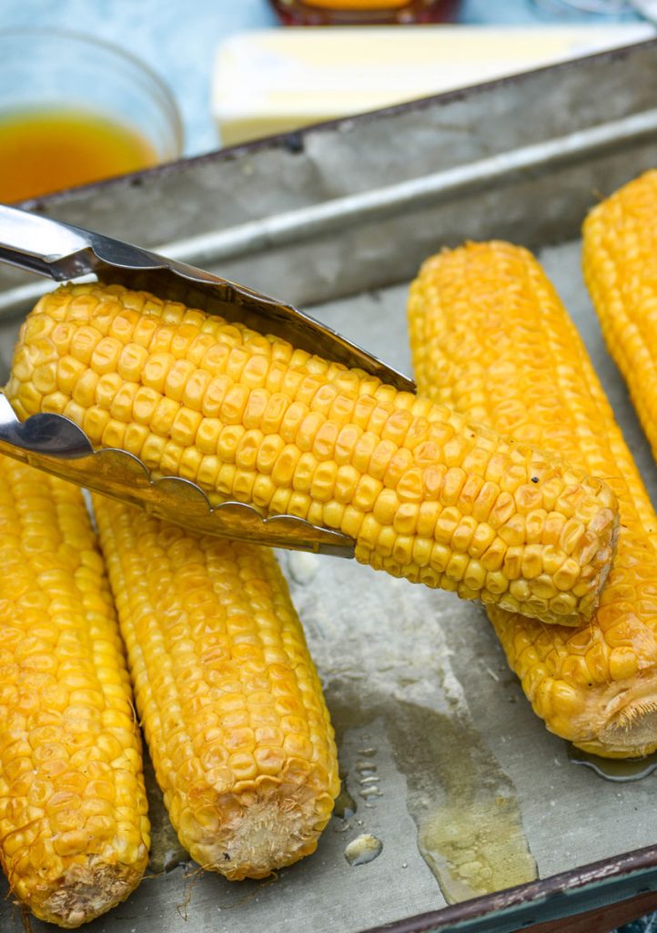 honey glazed smoked corn on the cob held aloft with metal tongs