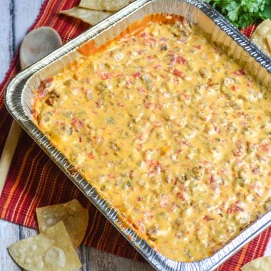 smoked queso dip in an aluminum foil baking pan with fresh tortilla chips and a bunch of cilantro in the background