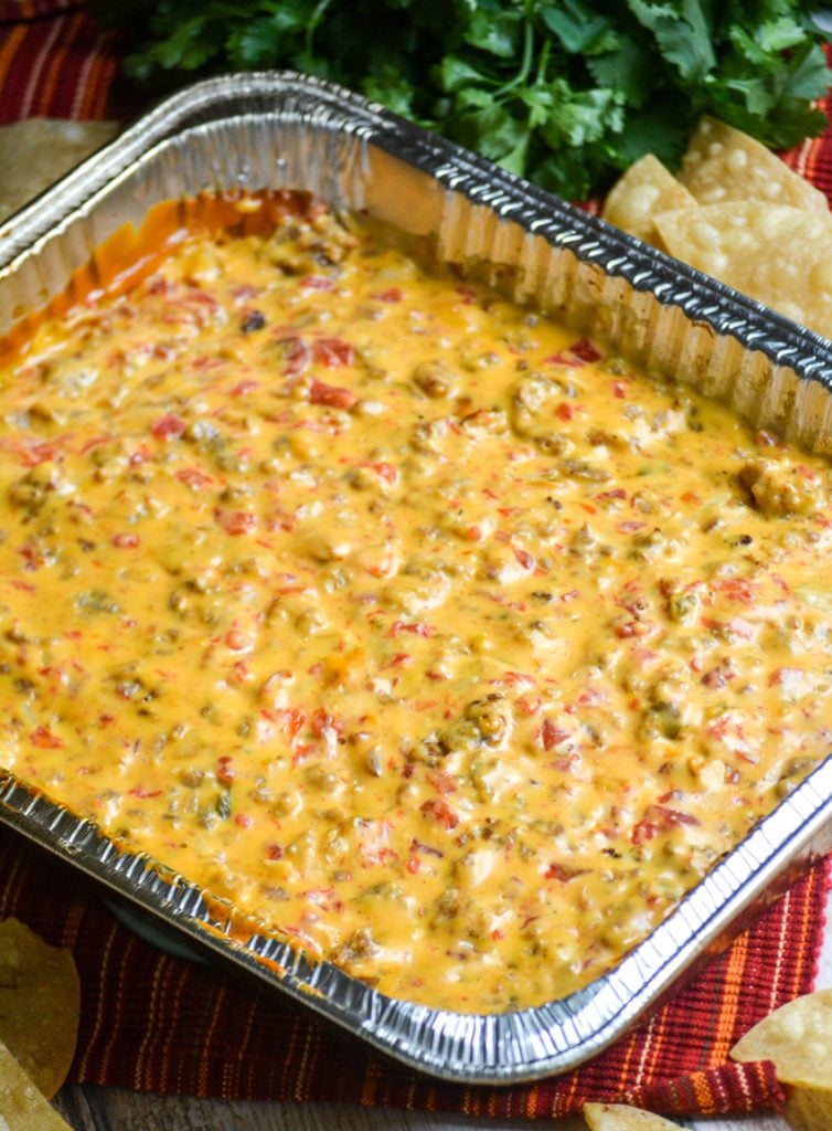 smoked queso dip in an aluminum foil baking pan with fresh tortilla chips and a bunch of cilantro in the background