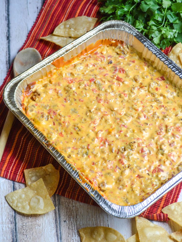 smoked queso dip in an aluminum foil baking pan with fresh tortilla chips and a bunch of cilantro in the background