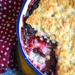 sweet dark cherry cobbler shown in a ceramic pie dish with a scoop removed