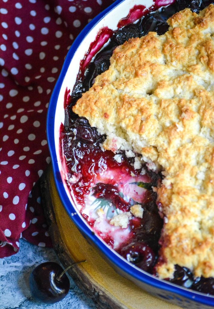 sweet dark cherry cobbler shown in a ceramic pie dish with a scoop removed