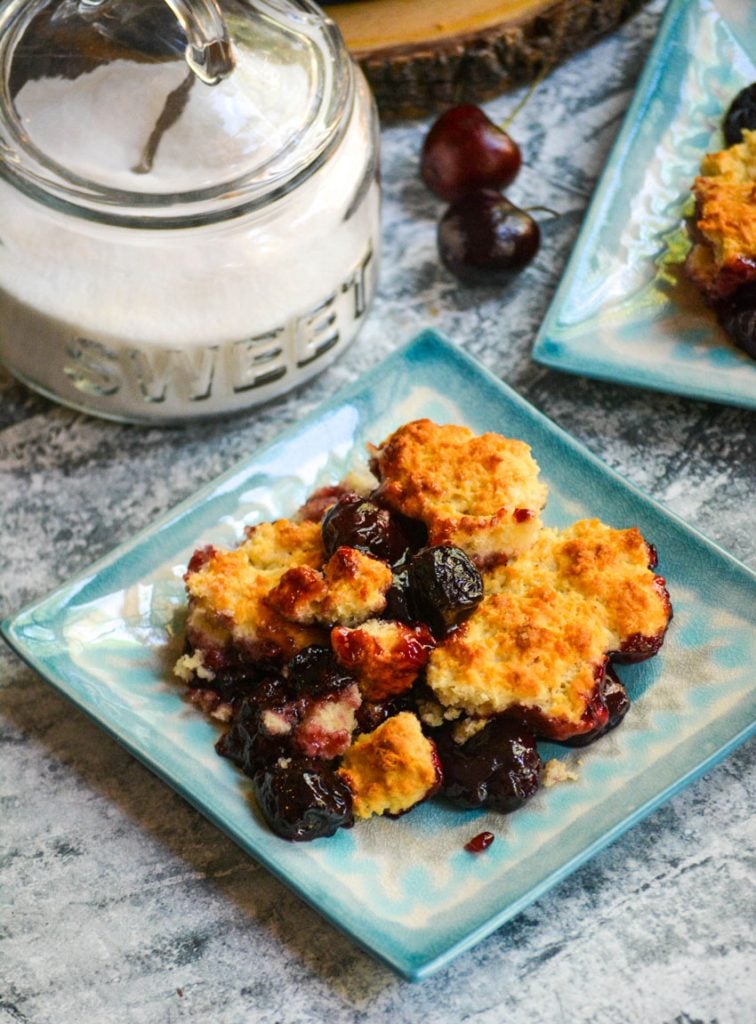 sweet cherry cobbler served on light blue plates with a sugar dish in the background