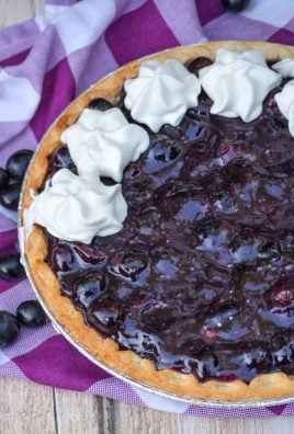 black grape pie with dollops of whipped cream on a purple checkered napkin
