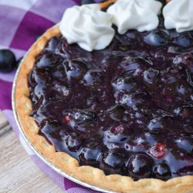 black grape pie with dollops of whipped cream on a purple checkered napkin