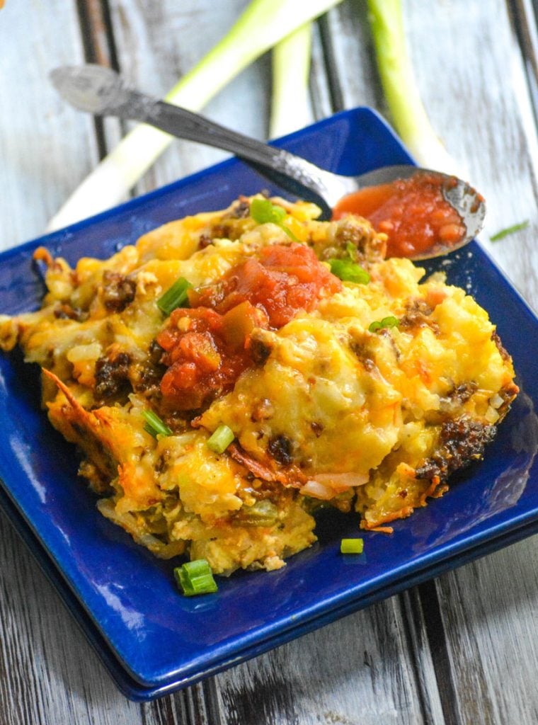 chile relleno casserole with chorizo shown on a blue square plate with a spoonful of picante sauce on the side