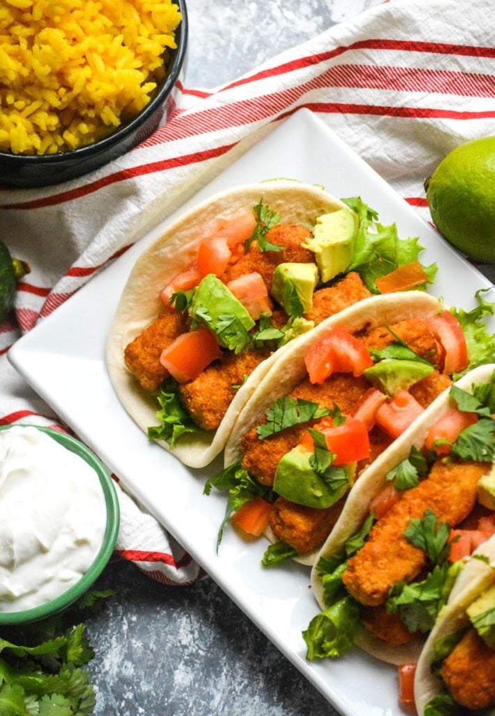 chili lime fish stick tacos in flour tortillas shown in a row on a white rectangular serving platter