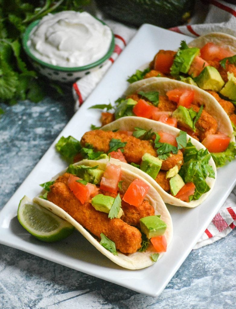 chili lime fish stick tacos in flour tortillas shown in a row on a white rectangular serving platter