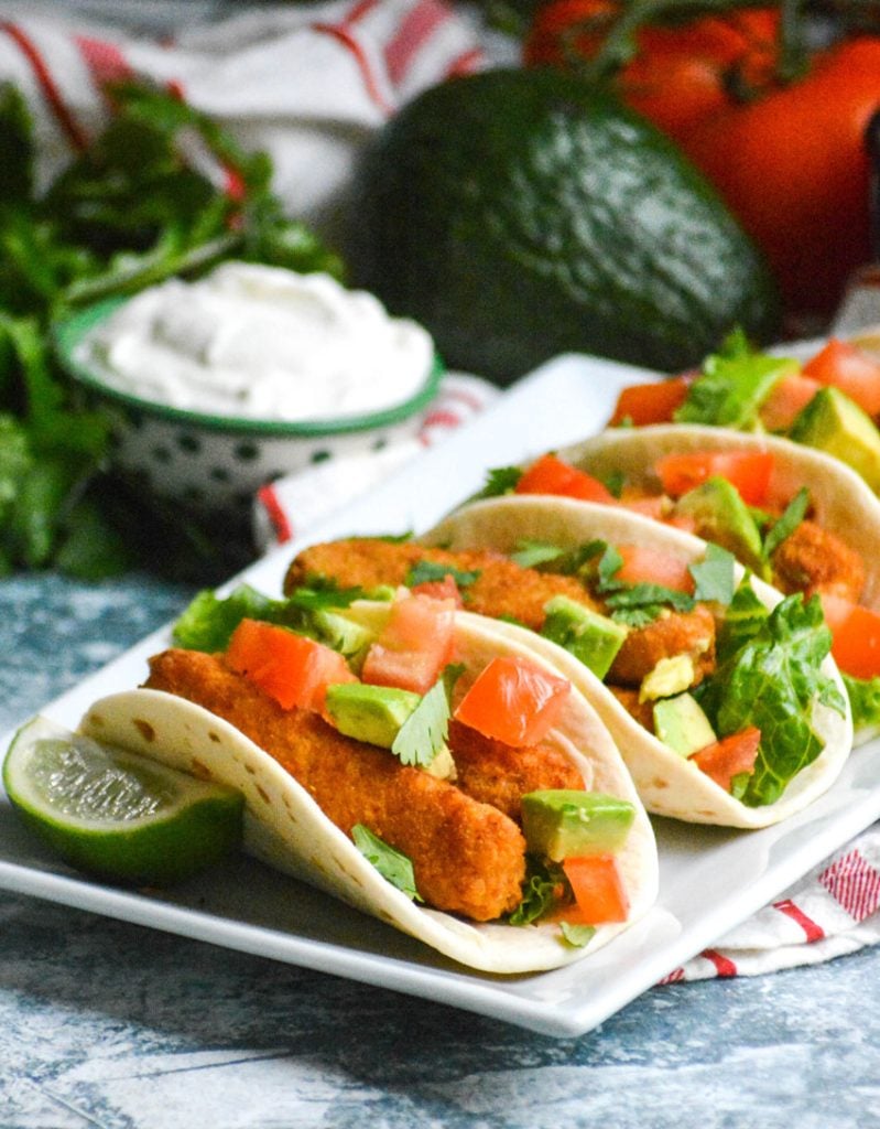 chili lime fish stick tacos in flour tortillas shown in a row on a white rectangular serving platter