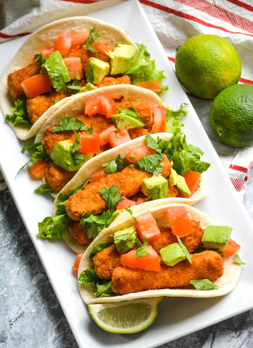 chili lime fish stick tacos in flour tortillas shown in a row on a white rectangular serving platter