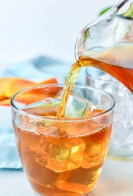 peach tea being poured over ice into a clear glass