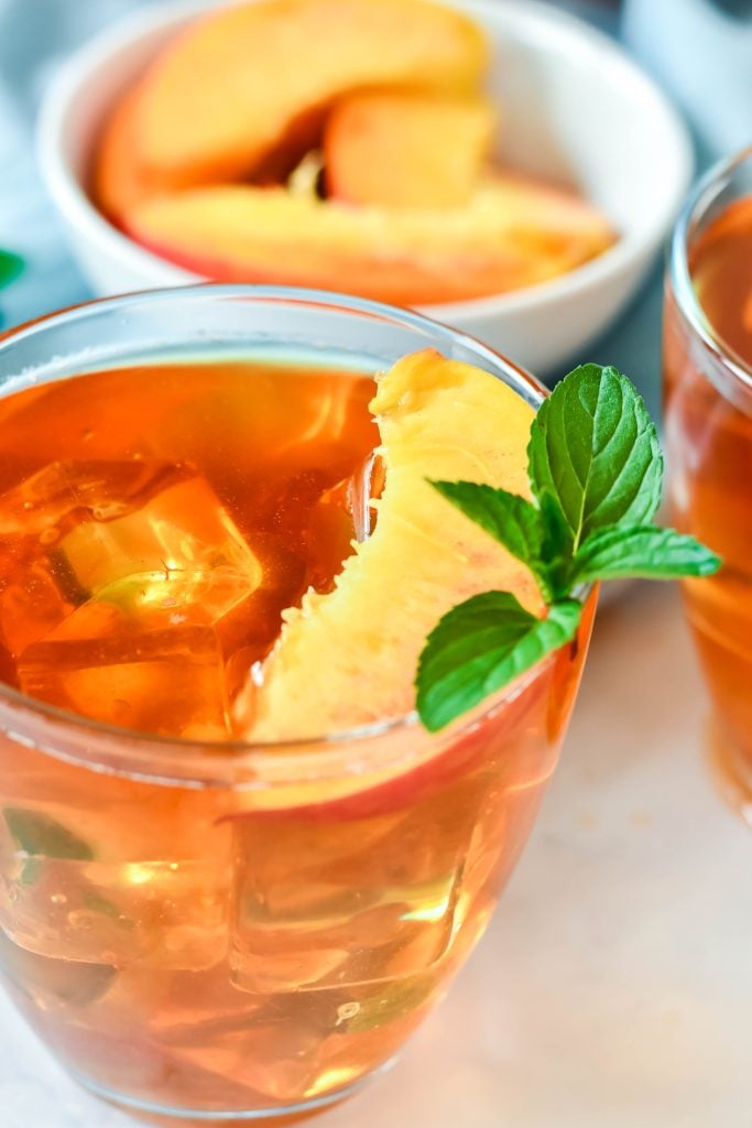 Southern Sweet Peach Tea Recipe served in clear glasses and garnished with fresh peach slices and a sprig of mint