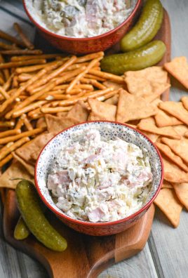 dill pickle wrap dip in a red bowl shown on a cutting board with pretzels & crackers ready to be served