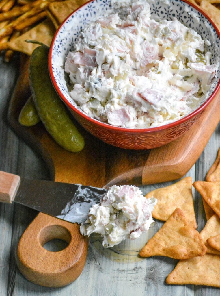 dill pickle wrap dip in a red bowl shown on a cutting board with pretzels & crackers ready to be served